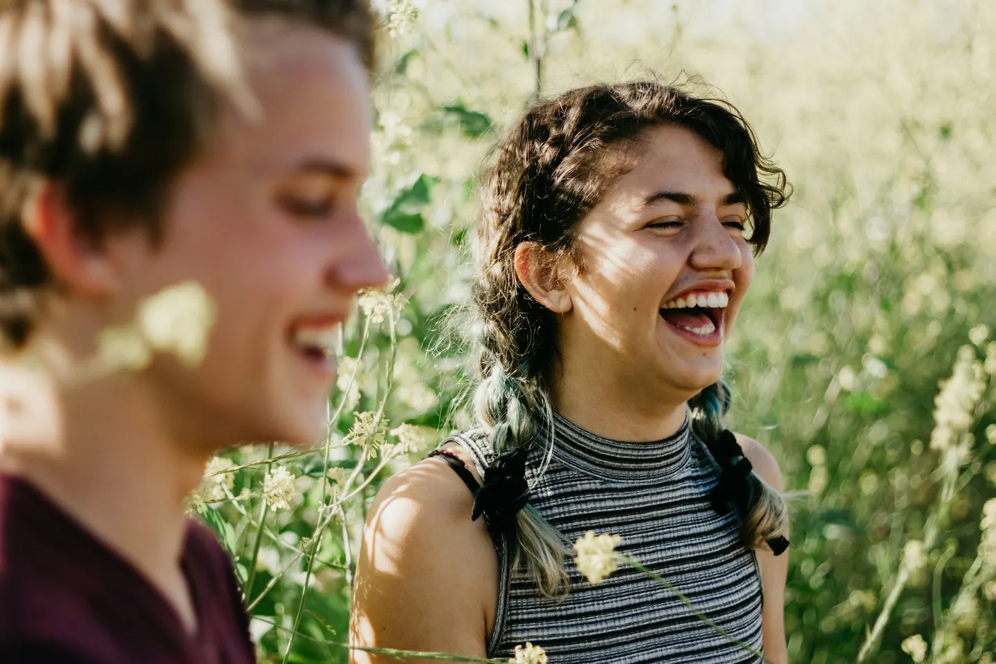 Two friends laughing together in a sunlit field of wildflowers